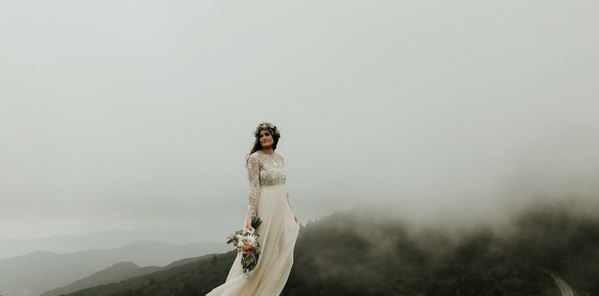 Joven novia de pie usando su vestido de novia. Tambien lleva un ramo y una corona de flores