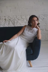 Video de modelo sentada en sofá azul mirando hacia el lado. En el video se puede ver su precioso vestido de novia compuesto por falda blanca larga + crop top de tirantas en tela de tul de margaritas doradas.