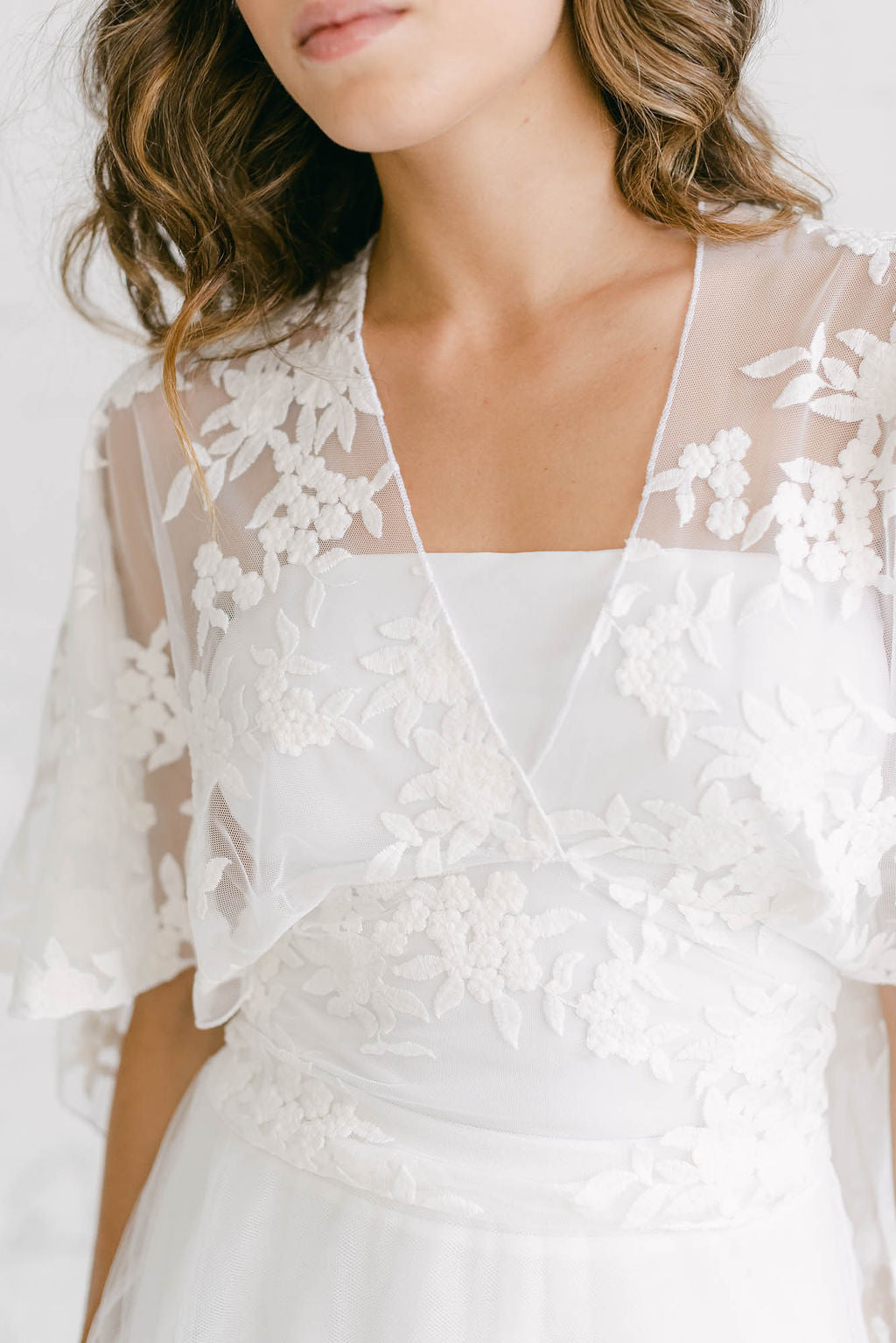 Detalle de una capa de tul de flores para novia, con escote en V y anudada a la cintura