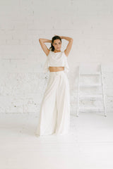 Modelo vestida como novia, de cuerpo entero y luciendo un pantalón de pierna ancha con un crop top. Este dos piezas es de estilo minimalista y moderno