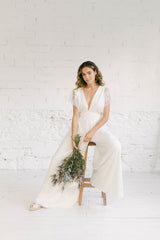 Modelo sentada en un taburete con un mono de novia con una sobrecapa de encaje ivory