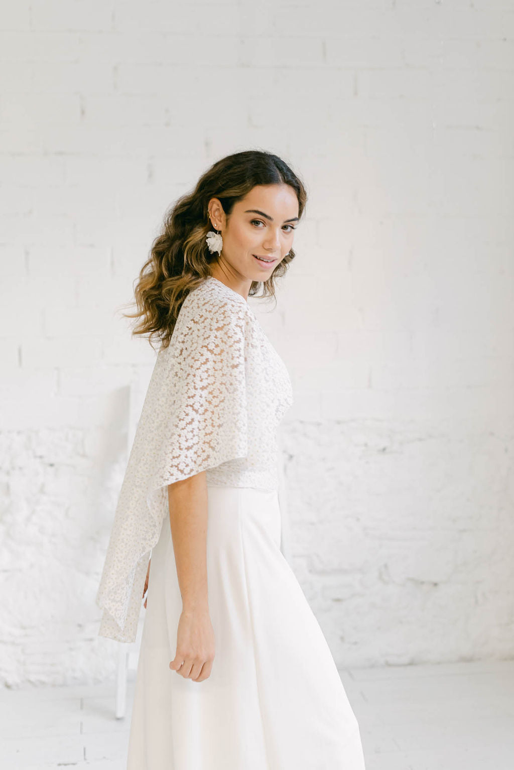 Novia de perfil luciendo un maravilloso pantalón palazzo. El efecto de perfil es como de falda. Está combinado con una capa en encaje de flores.