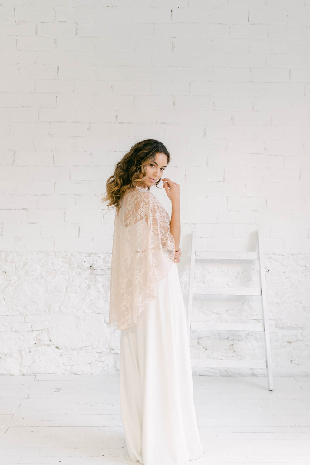 Modelo de espaldas luciendo un maravilloso vestido capa novia dos piezas. El accesorio clave es una capa maravillosa de encaje