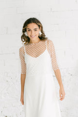 Mujer sonriendo a cámara llevando un vestido de novia con manga desmontable. La manga es tres cuartos y de tul de flores