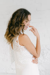 Foto en detalle de una mujer sonriendo de perfil. Tiene la mano colocada encima de su vestido de novia hippie chic sin mangas. El crop top es de tul bordado.