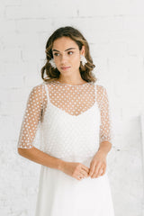 Modelo sonriendo suavemente de lado, que lleva un vestido de novia lencero con manga. Tiene escote en V, espalda baja y esta hecho de crepe