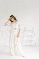 Modelo de pie y sonriendo ligeramente. Combina en su vestido dos piezas novia un pantalón palazzo con un top de flores