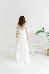 Modelo de espaldas y de cuerpo entero. Luce un abrigo de encaje que con una cola incorporada que es pura magia. Este vestido de novia es perfecto para las chicac bohemias.