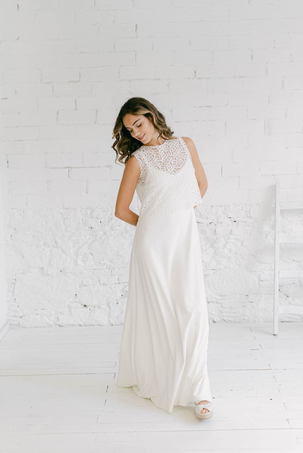 Novia de cuerpo entero y caminando hacia cámara. Luce un vestido de novia sin mangas que le queda ideal. El corte es en A y el estilo es hippie