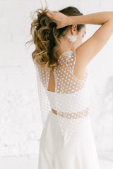 Modelo con crop top con espalda abierta y manga corta en tela de tul de encaje en florecitas blancas. La modelo está recogiéndose el pelo con una coleta.