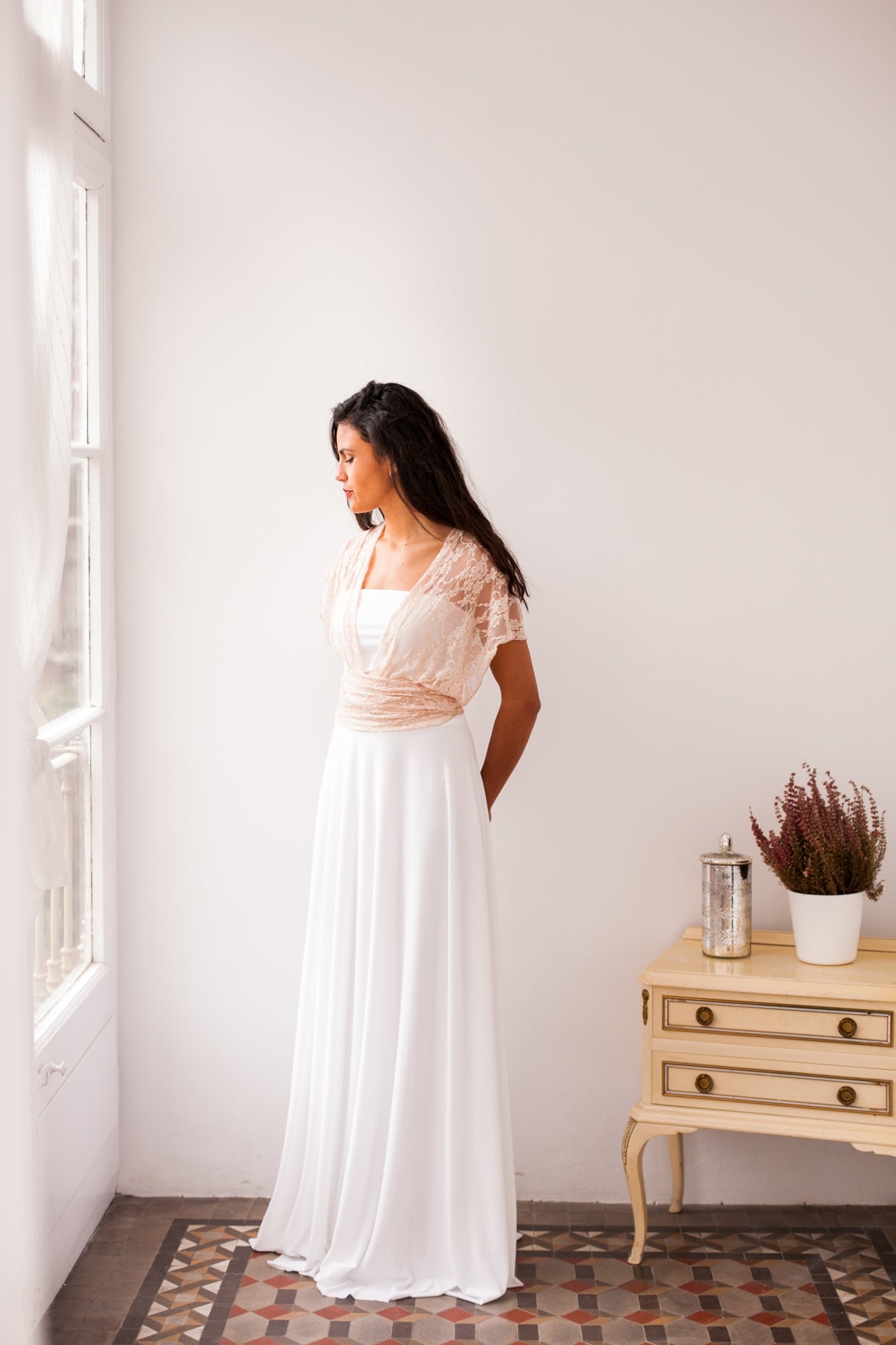 Modelo parada con los brazos hacia atras. Luce una combinacion de falta y bolero beige para su vestido de novia