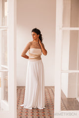 Modelo vista desde el exterior de la habitación, con su falda de novia y un bolero beige de tul. Posa con su brazo derecho en su espalda y su mano izquierda en su cabeza