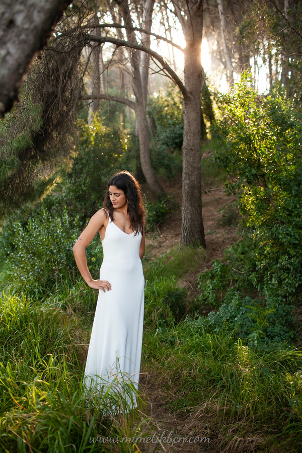 Una novia radiante de pie en un hermoso bosque, llevando un elegante vestido de novia blanco de Marie