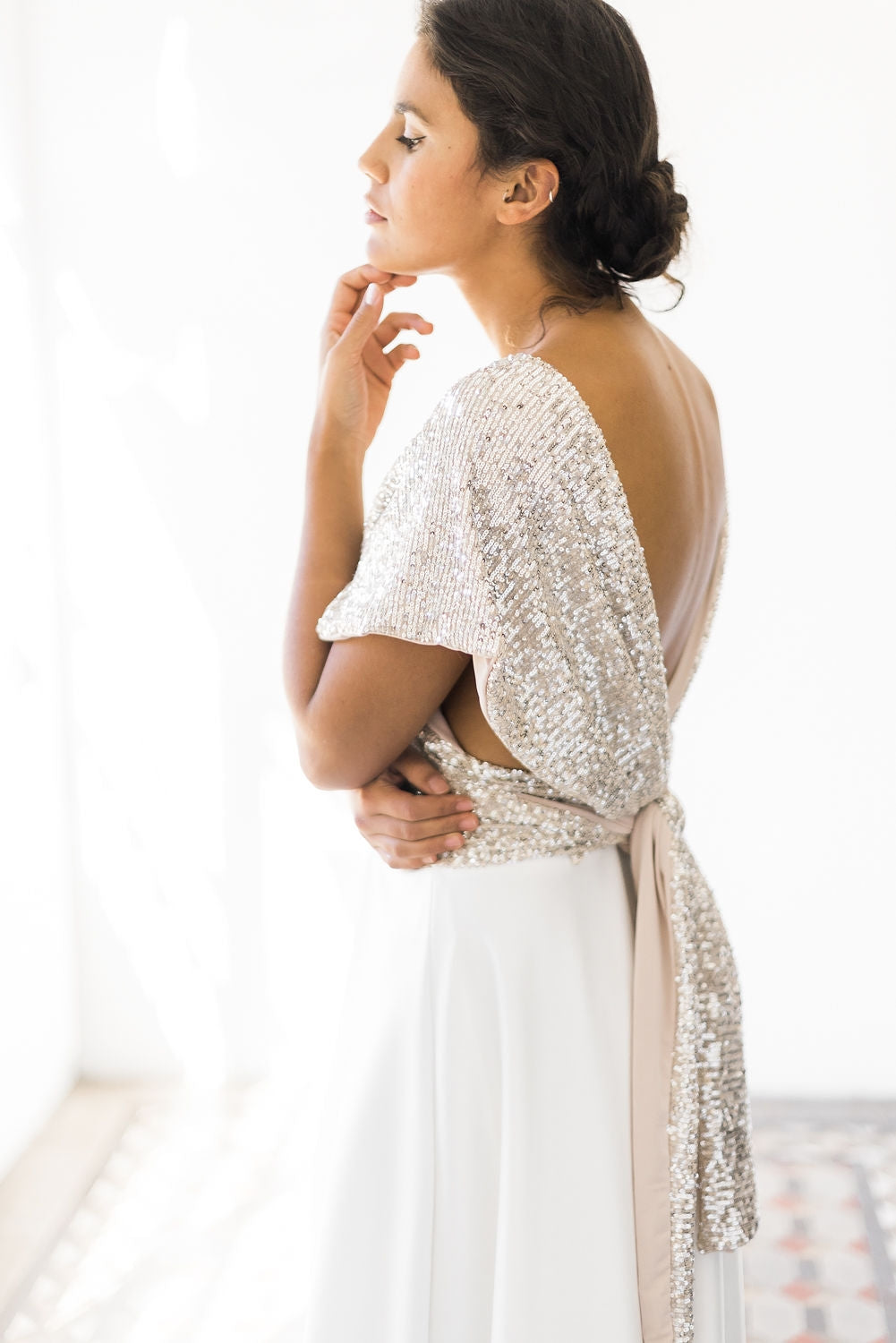 Modelo luciendo su top de lentejuelas con su vestido de novia, posando de costado y tocando su cara con su mano