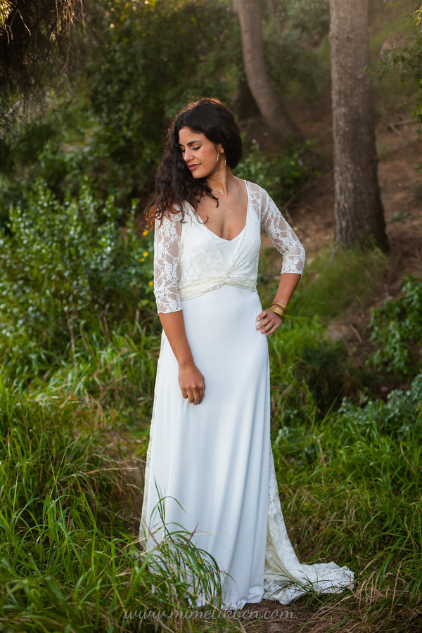 La novia se destaca en medio de un bosque, vistiendo un encantador vestido de novia blanco de Marie, complementado con un delicado bolero de encaje