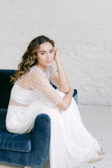 Foto de modelo más de cerca con crop top de mangas tres cuartos en tela de tul transparente y falda de encaje de florecitas blancas.