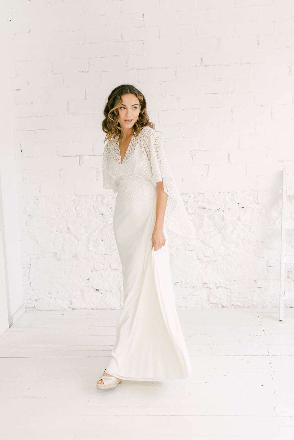 modelo frente a cámara con vestido de novia blanco lencero con capa corta en margaritas doradas
