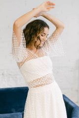 Modelo vestida con traje de novia dos piezas con top bolero de mangas con volantes y falda en telas de tul transparentes de florecitas
