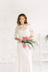 Modelo chica sonriendo a cámara sujetando flores rosas en la mano y con vestido de novia con top de encaje de flores