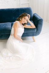 Modelo sentada en el suelo apoyada en sofá de color azul añil. Vestido dos piezas con tela de encaje de tul transparente florecitas blancas,