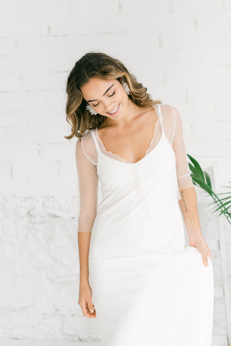 Foto más ampliada de la modelo sonriendo al suelo con vestido de novia con top transparente y pendientes a juego con el mismo.