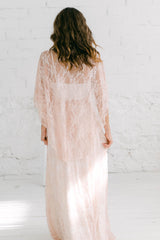 Modelo de espaldas a la cámara con vestido dos piezas de encaje color rosa, el top acaba en una capa midi rosa cuarzo.