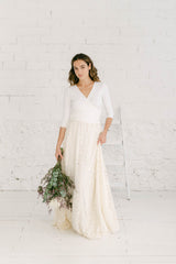 Chica con vestido de novia dos piezas estilo bohemio con vestido Frida blanco de manga tres cuartos y escote en V + falda de enaje con bordado de flores crema.