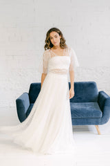 Modelo con vestido de novia al vuelo formado por : top palabra de honor blanco + bolero de mangas escalonadas en tela de tul transparente de florecitas blancas y falda blanca con sobrefalda en misma tela que el top.