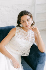 Modelo chica apoyada en sofa azul, con vestido de novia largo con top de flores blancas.
