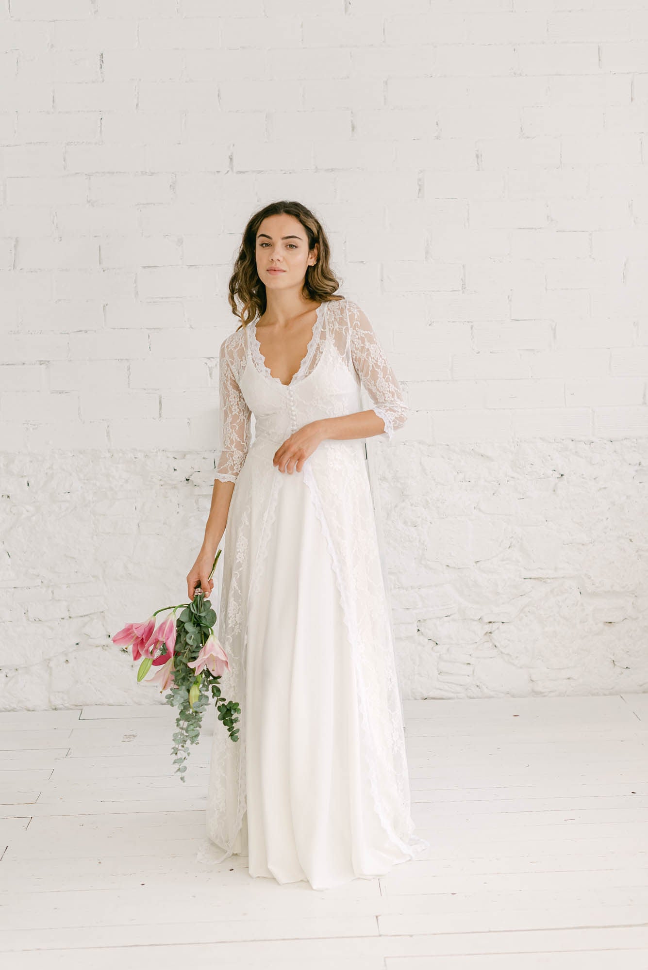 Modelo frente a cámara con vestido de boda dos piezas formado por falda blanca larga y crop top marie de tirantas con abrigo largo de cola blanca.