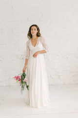 Modelo frente a cámara con vestido de boda dos piezas formado por falda blanca larga y crop top marie de tirantas con abrigo largo de cola blanca.