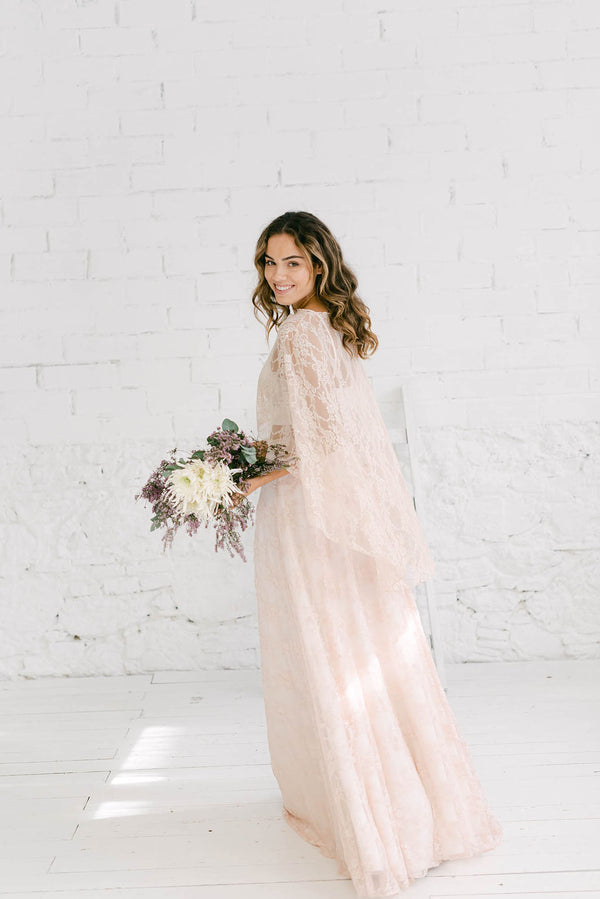 modelo chica de espaldas a la cámara y mirando hacia atrás con ramo de flores en la mano. Vestido de novia en color rosa cuarzo.
