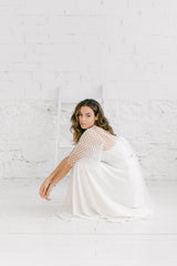 Modelo agachada en el suelo con los brazos estendidos delante con falda blanca y top bolero con mangas de volantes en tela de florecitas blancas.