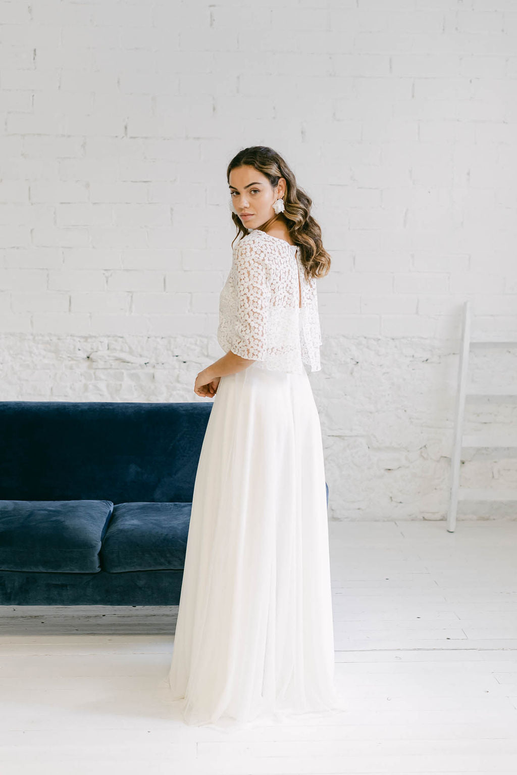 Modelo de espaldas a cámara mirando atrás con falda de novia de tul blanca y crop top con espalda abierta de margaritas doradas.