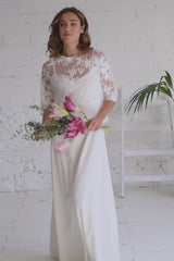 Video de modelo andando a cámara con crop top de manga tres cuartos en flores de encaje blanco. La modelo lleva un ramo de flores rosas en la mano.