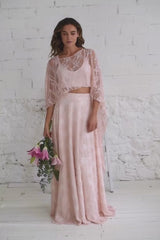 Video de modelo andando a cámara con flores rosas en la mano. Vestido de boda de encaje rosa cuarzo y capa maxi.