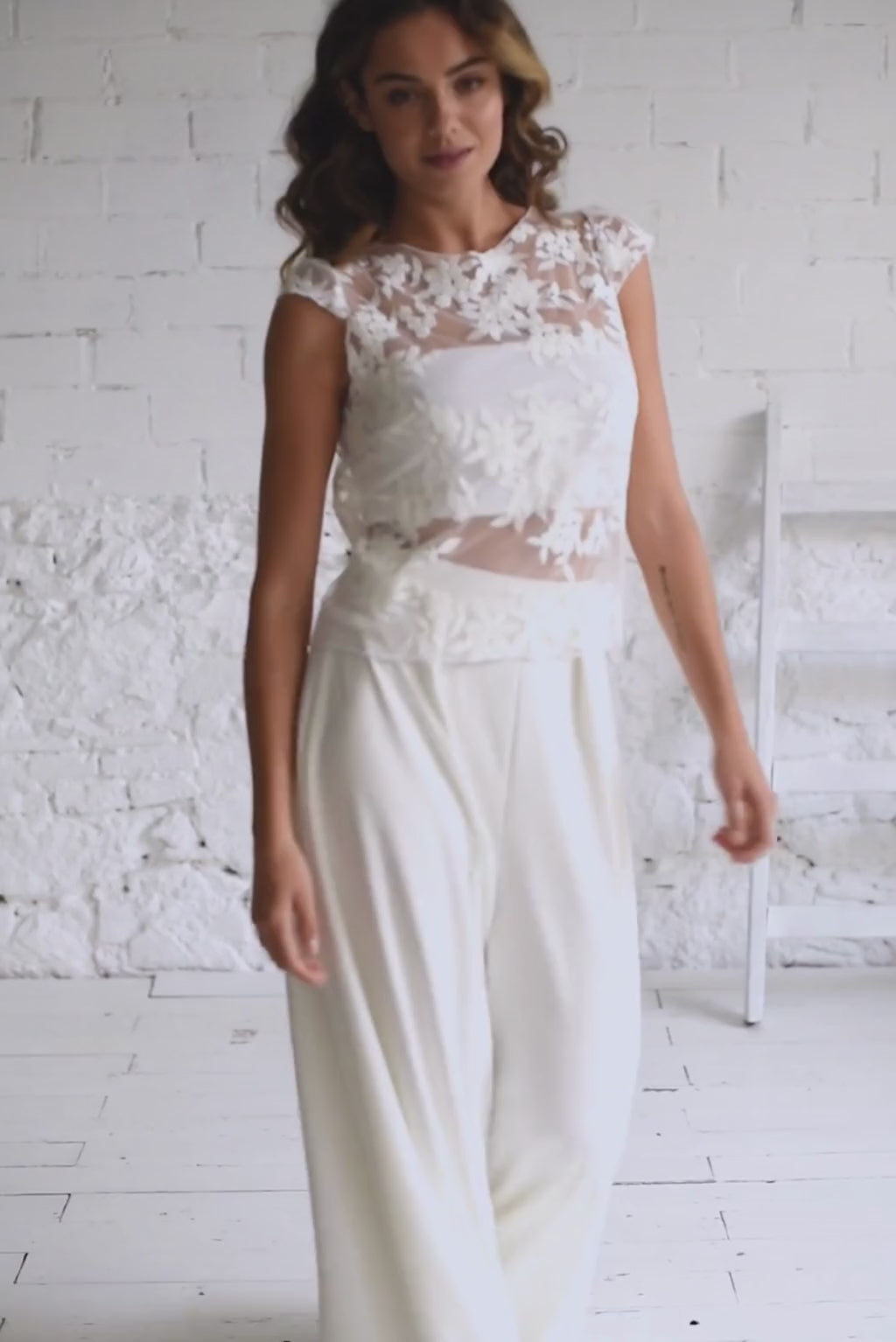 Video de modelo chica con traje de novia dos piezas con pantalon palazzo en crepe y crop top espalda abierta en tul bordado de flores blancas.