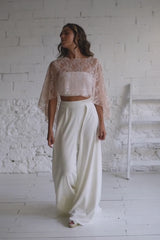 Modelo chica luciendo un espectacular vestido de novia pantalon con preciosa capa corta en tela de tul de encaje en rosa cuarzo.