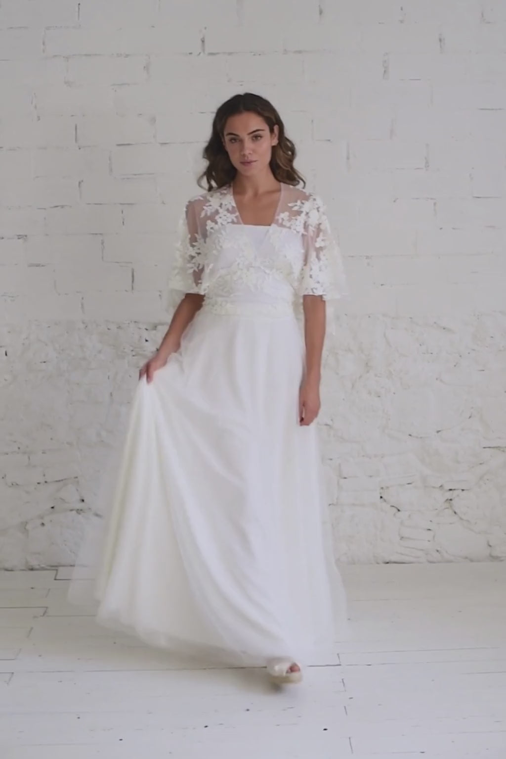 Video de modelo andando a cámara moviendo la falda del vestido de novia con top de encaje bordado de flores blancas.