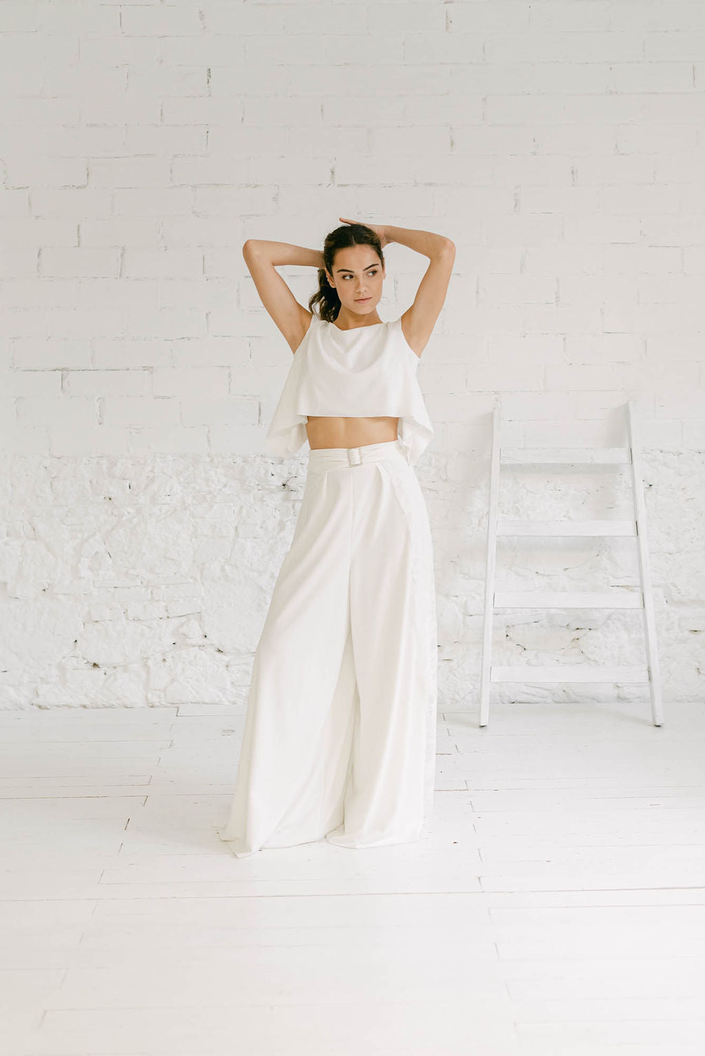 Modelo vestida como novia, de cuerpo entero y luciendo un pantalón de pierna ancha con un crop top. Este dos piezas es de estilo minimalista y moderno
