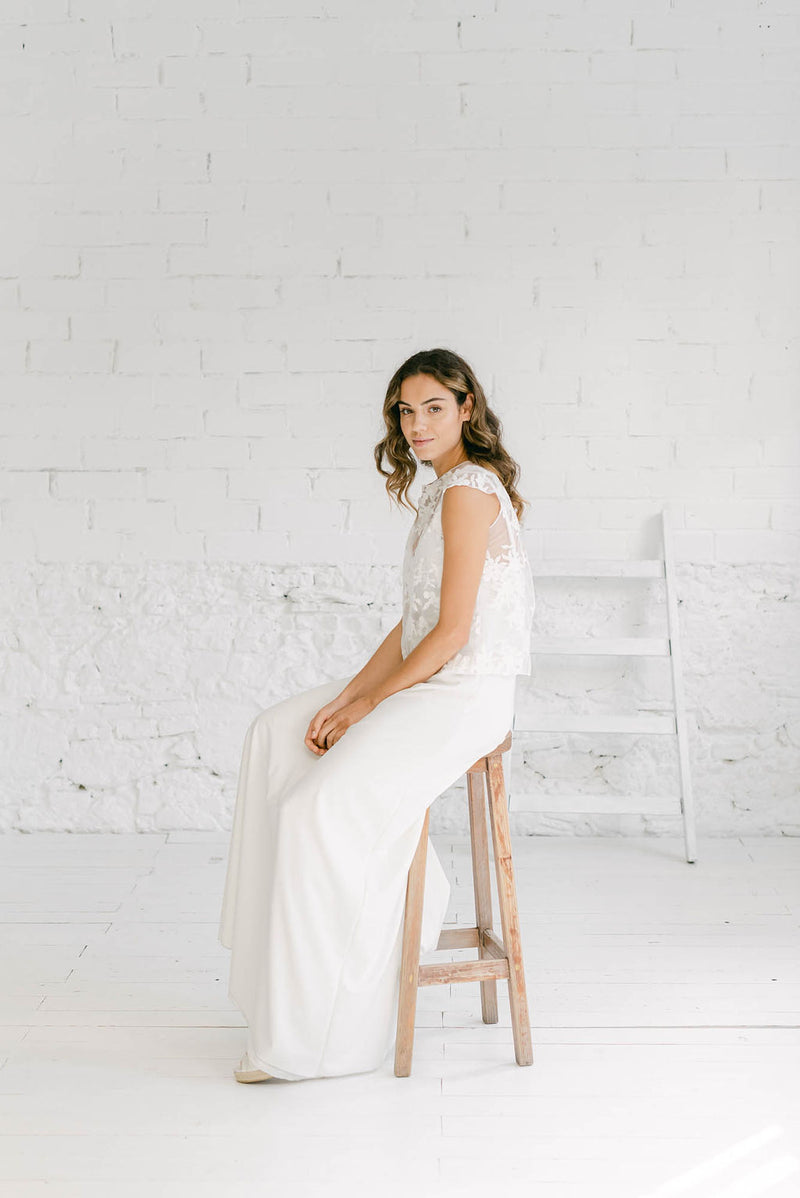 Novia sentada en un taburete con un estilo minimalista. Lleva un crop top para novia vestido dos piezas