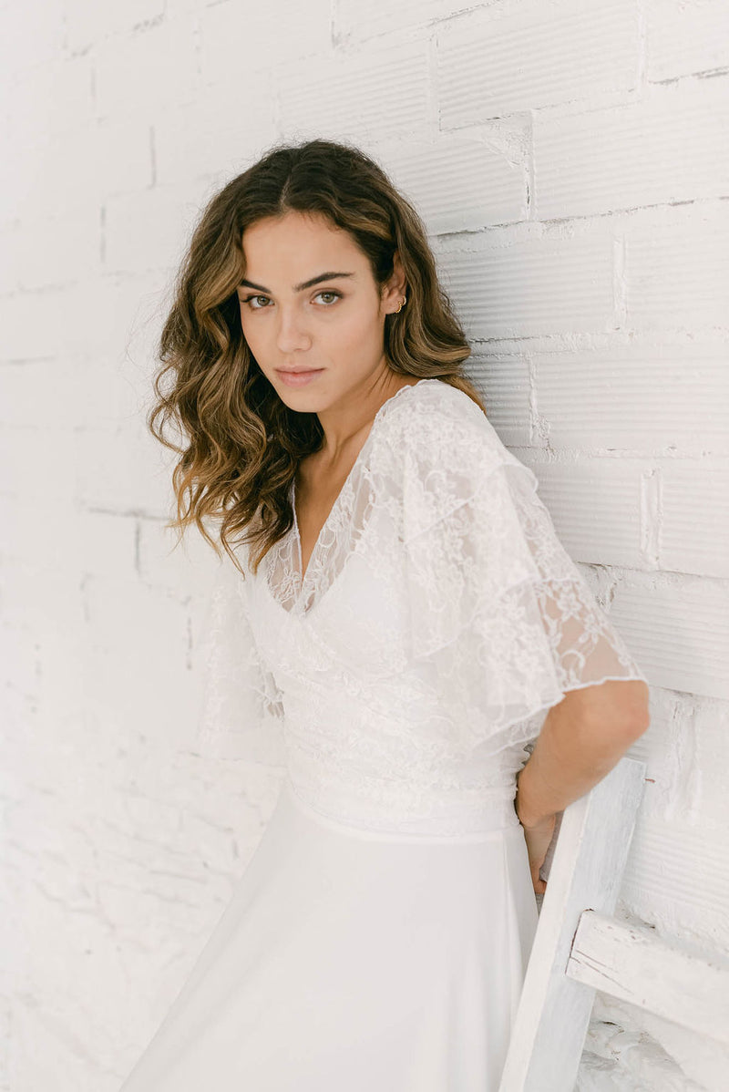 Modelo apoyada en la pared vestida de novia con un conjunto de vestido sencillo minimalista y torera para novia