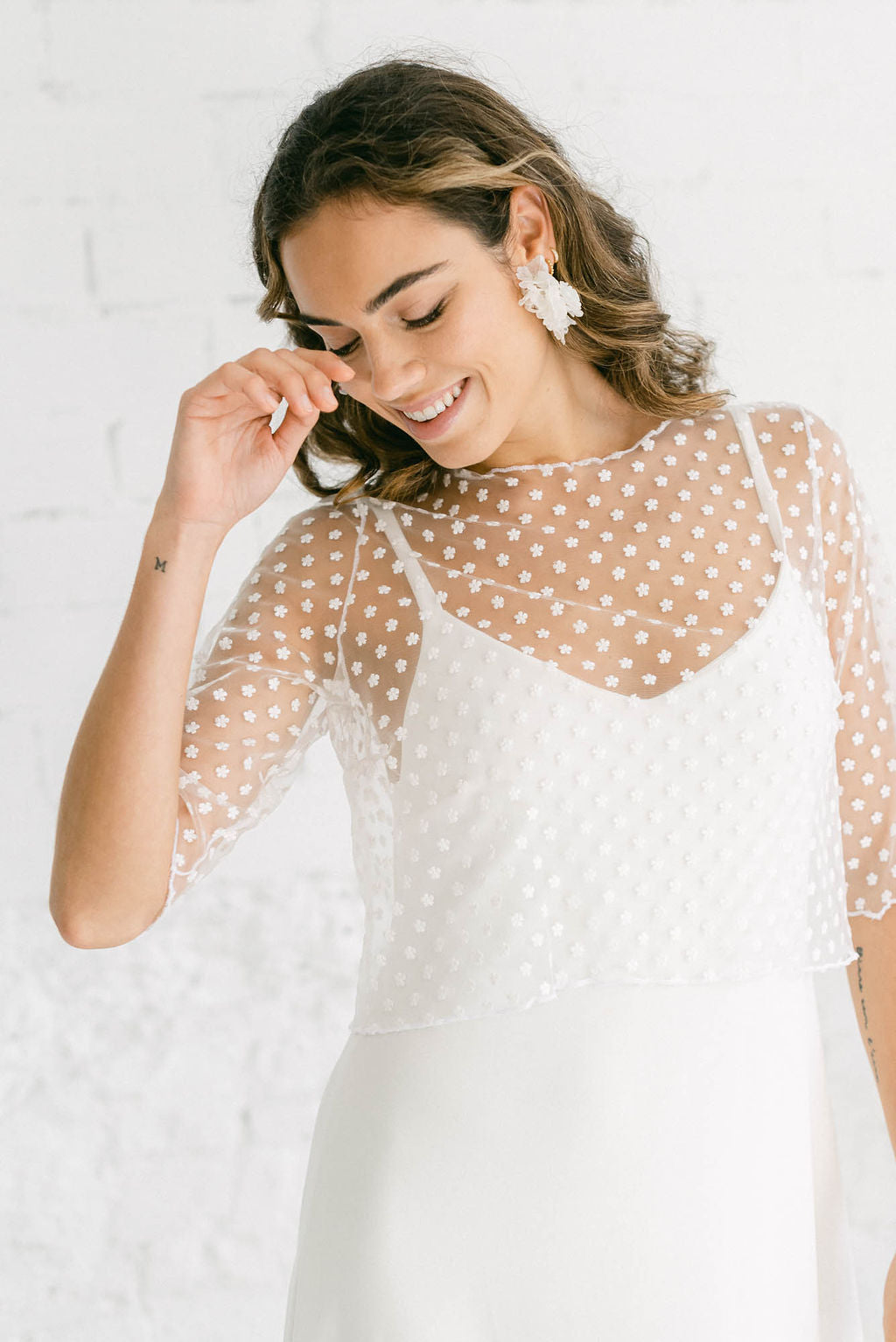 Modelo fotografiada de cerca con un vestido de novia estilo lencero. Encima de él lleva un crop top que sirve como manga desmontable, ya que puede ponerse o quitarse a lo largo de la boda