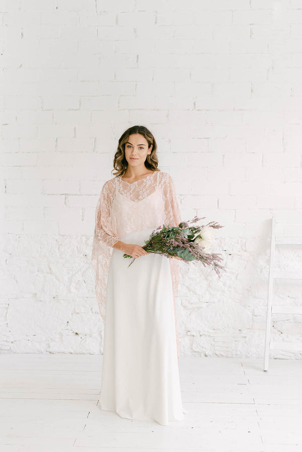 Modelo de frente luciendo un vestido de novia moderno con capa de encaje rosa. En las manos lleva un ramo de flores bohemio. Este estilo, muy sencillo, es perfecto para las novias que quieren sentirse auténticas.