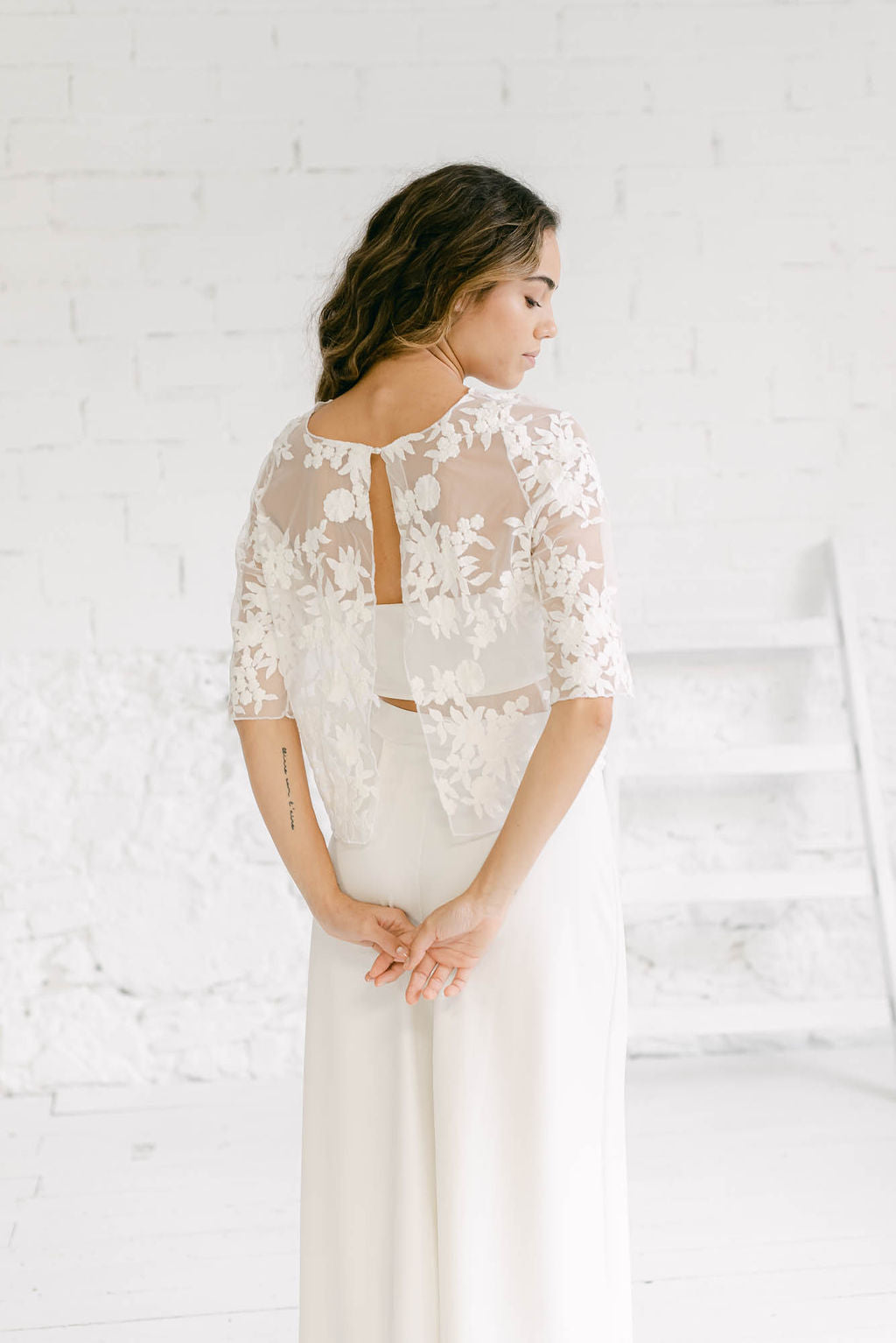 Modelo vestida como novia y fotografiada de espaldas. Lleva una combinación que nos fascina: un pantalón, un tube top y un crop top de flores. Es el vestido dos piezas perfecto