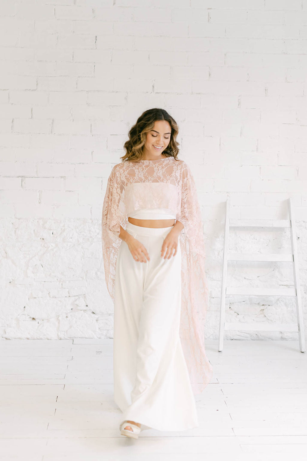 Novia sonriendo y de cuerpo entero. Lleva una combinación perfecta como vestido novia civil: pantalones, tube top y capa de encaje