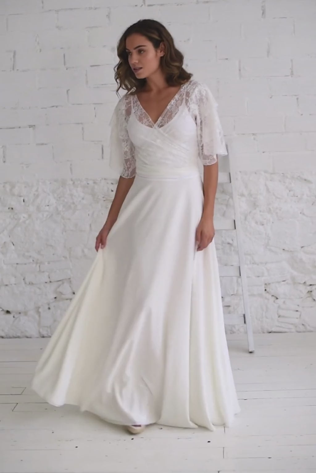 Video de modelo andando a cámara con vestido de novia blanco cómodo y de tirantes; con bolero de encaje blanco con escote en V.