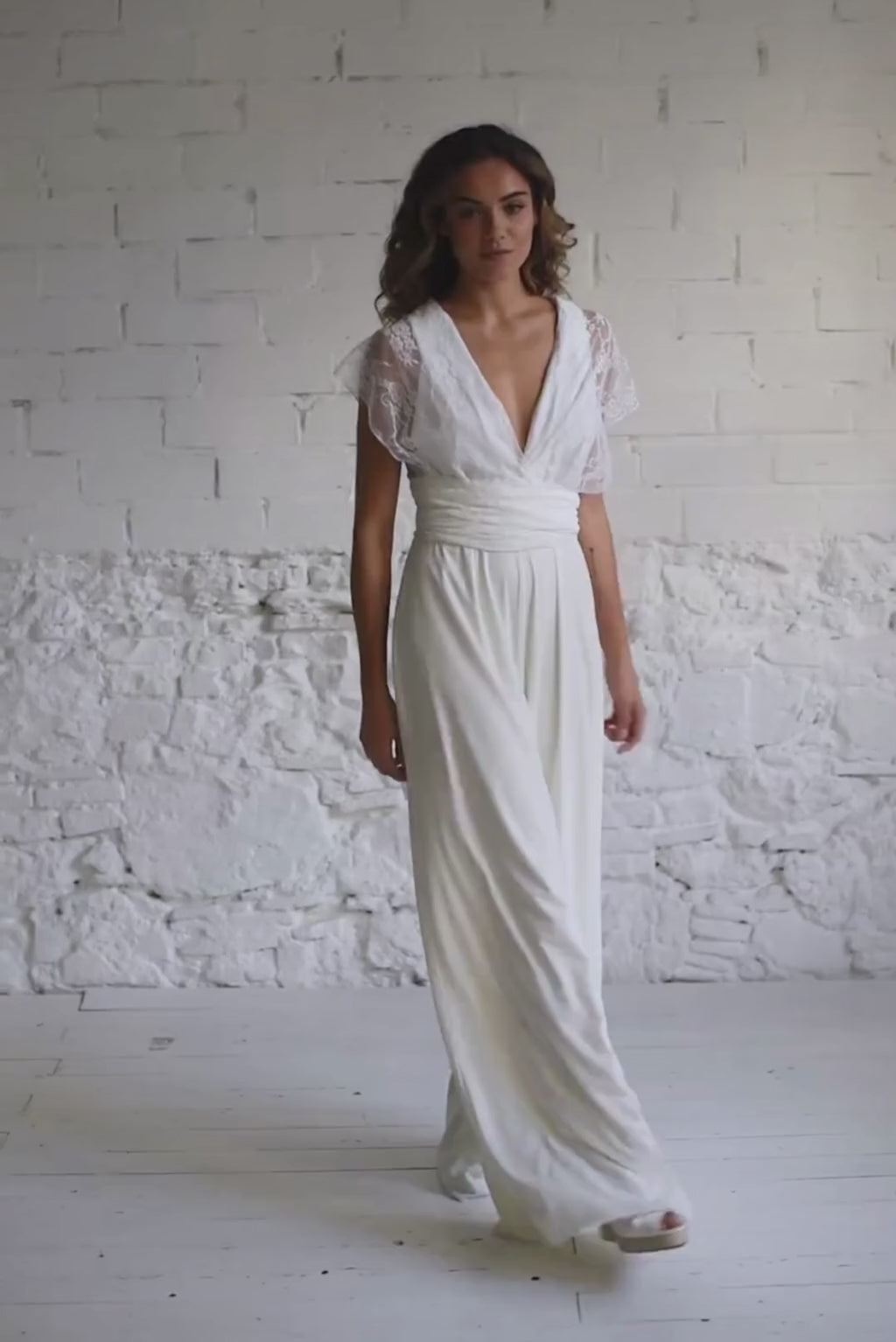 Video de modelo andando a cámara y tocándose el pelo. En este video la modelo lleva el mismo traje de novia formado por un mono largo con escote en V y unas straps de encaje rodeando el pecho y haciendo una X en la espalda.