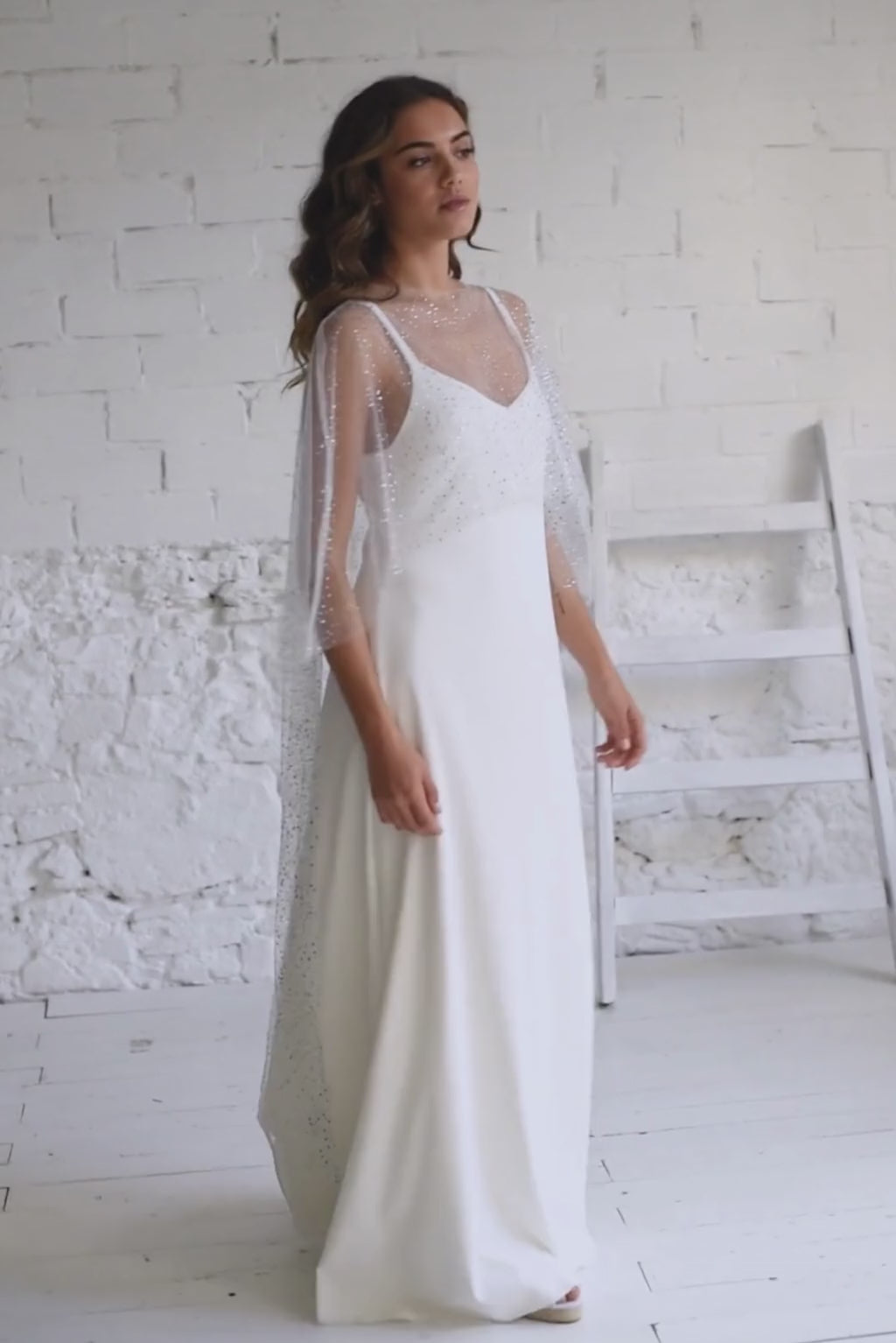 Video de modelo de pie con un vestido brillante sencillo novia. Combina un vestido lencero con una capa de tul brillante