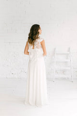 modelo de espaldas totalmente mirando hacia la izquierda con vestido de novia largo blanco y crop top donde podemos observar la apertura en la espalda.